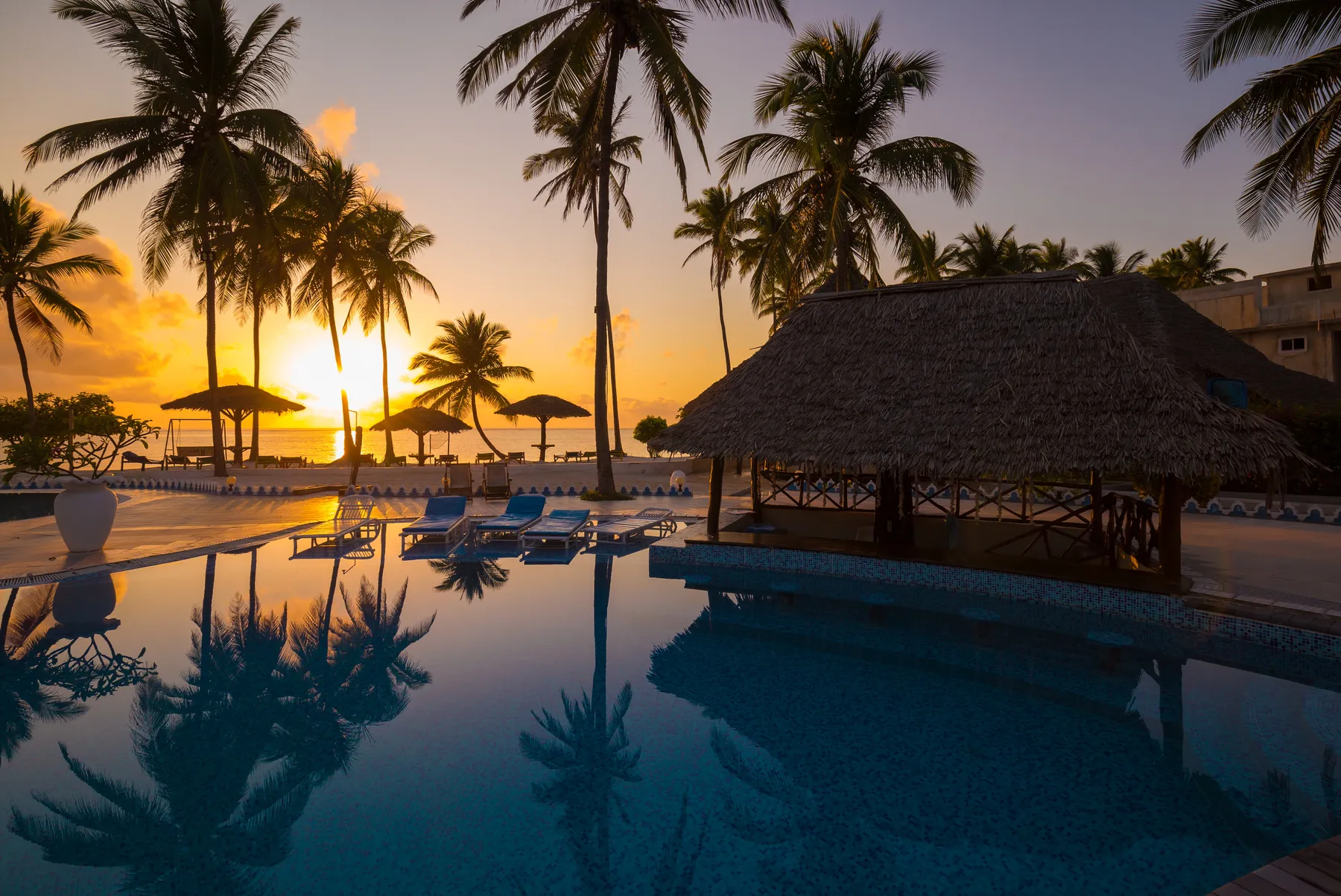 Palms and a thatched beach bar reflected at sunset on Zanzibar